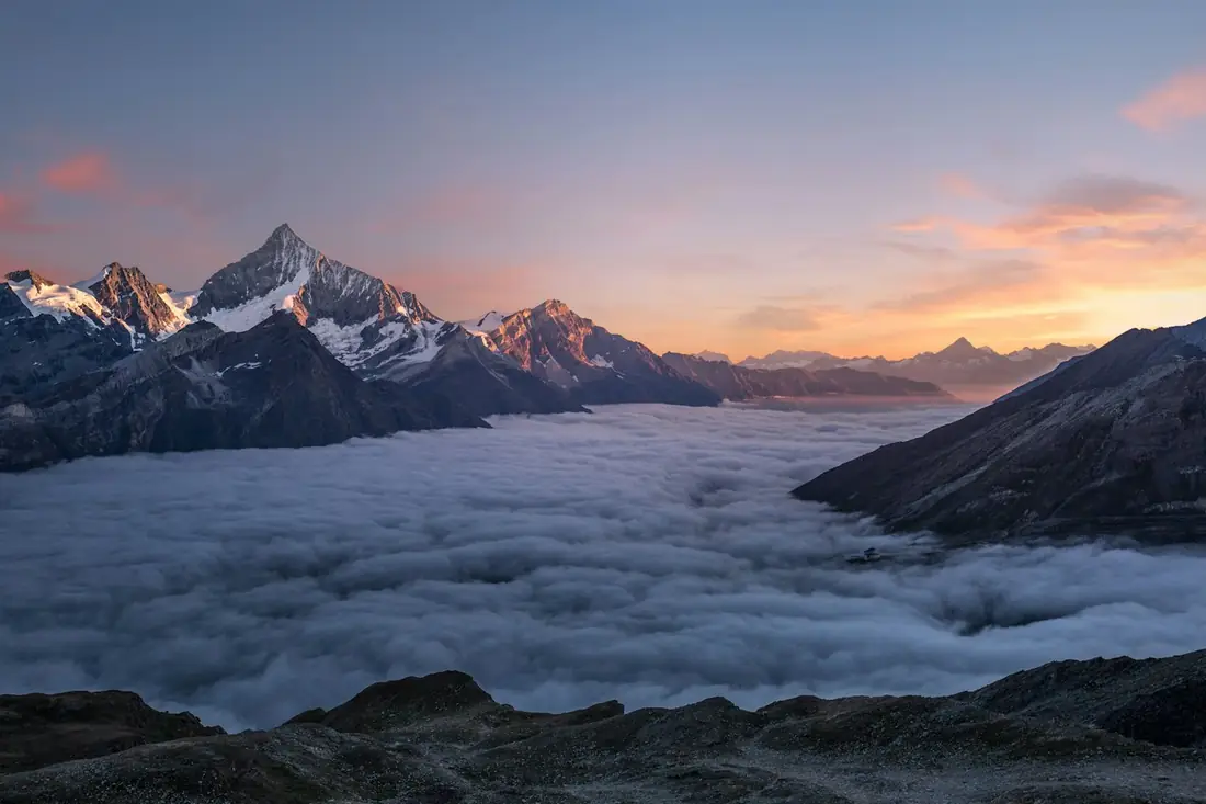 Lautan awan di bawah deretan puncak gunung saat senja
