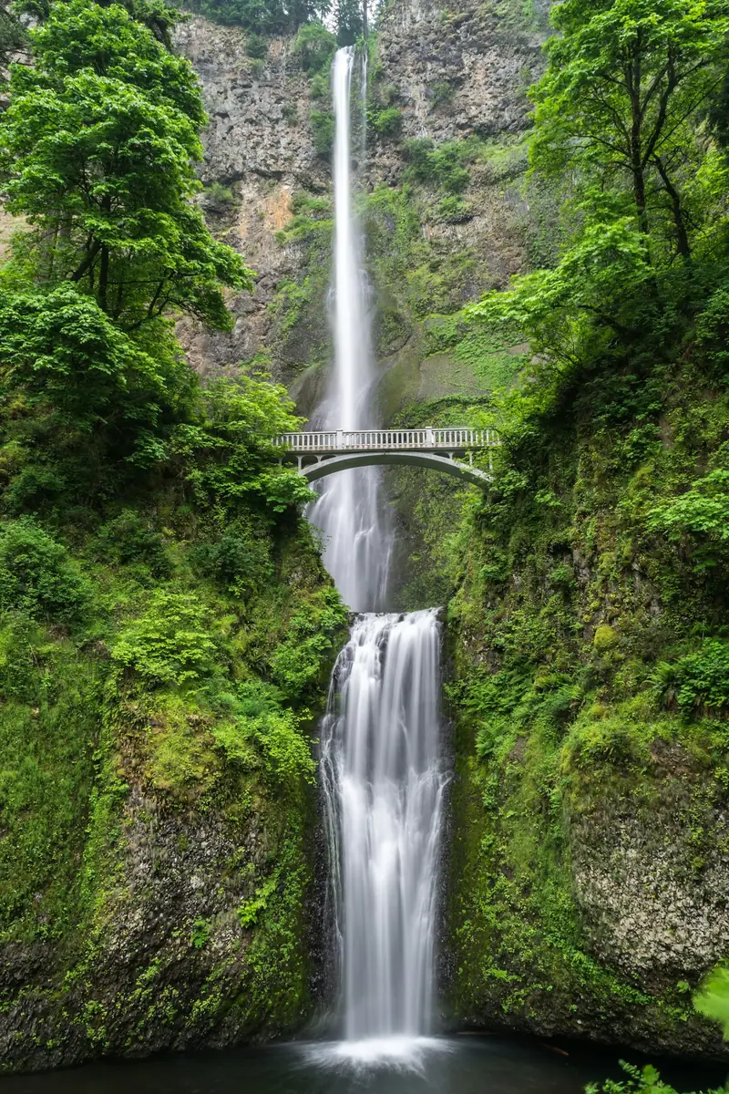 Air terjun tinggi bertingkat diapit tebing hijau